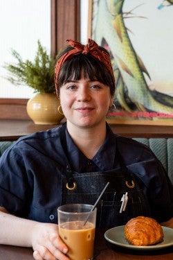 Zoe seated at a restaurant booth with coffee and a pastry