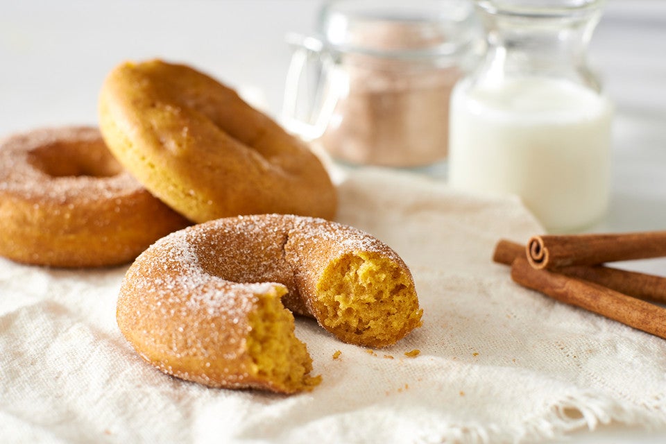 A few freshly baked cakey pumpkin donuts next to a glass of milk and a few cinnamon sticks.