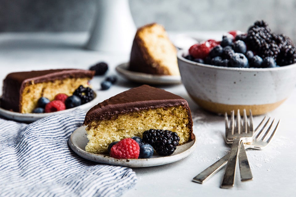 Two slices of yellow cake topped with fudge frosting on plates, garnished with fresh berries