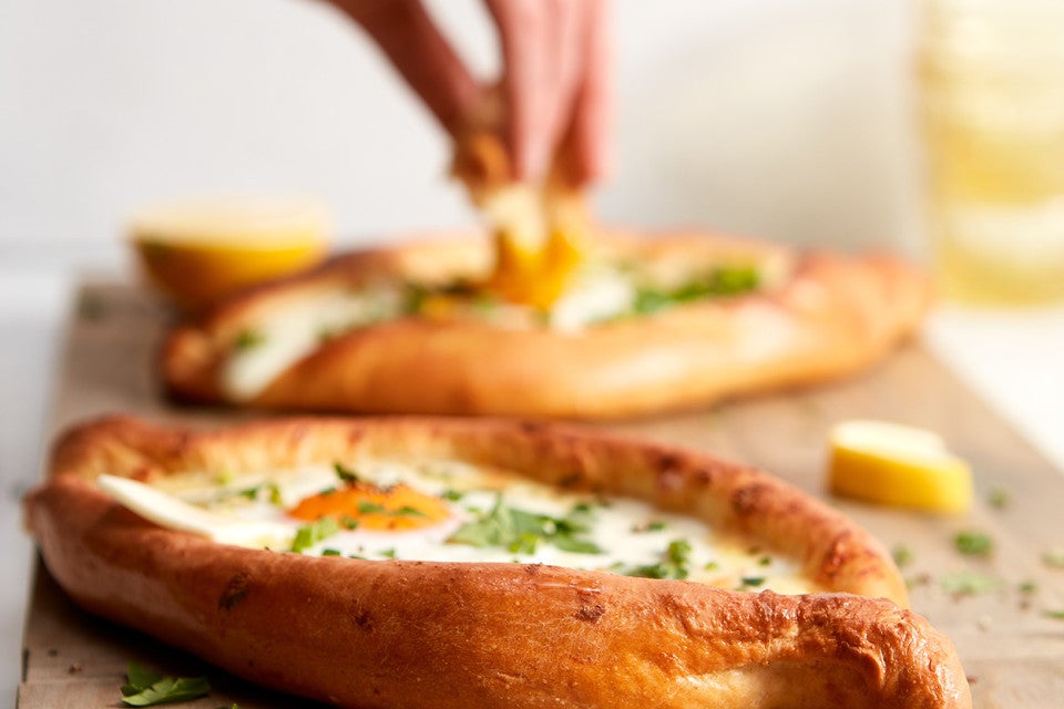 A hand dipping a piece of bread into the soft yolk of khachapuri (Georgian Cheese Bread)