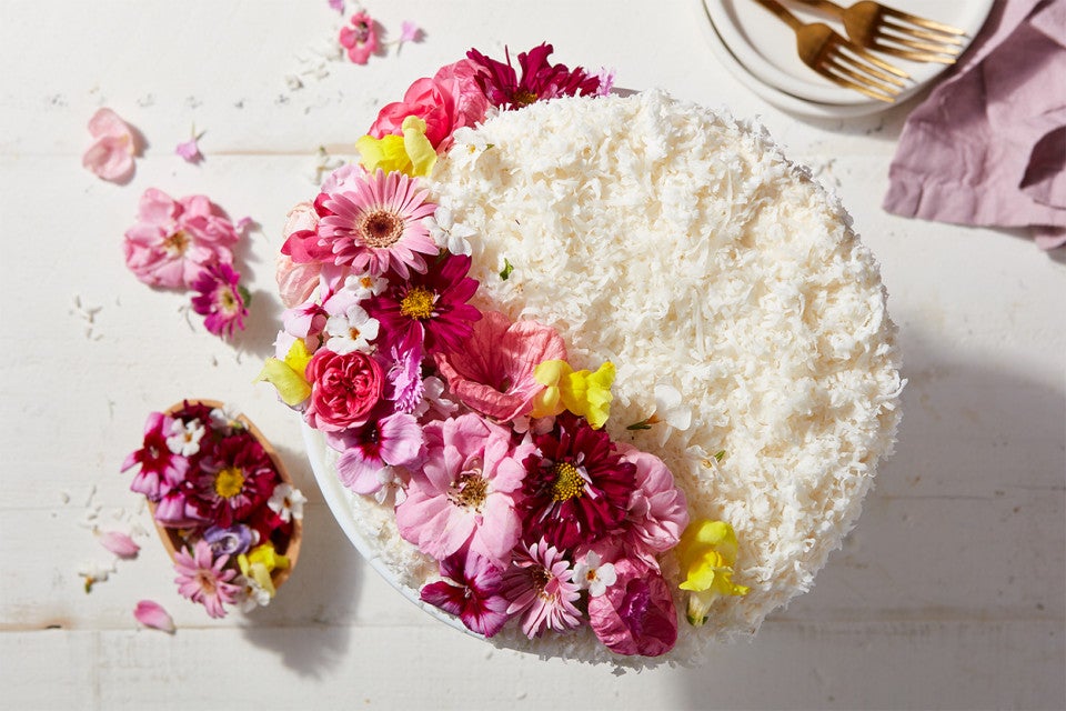 A whole Old-Fashioned Coconut Cake coated in shredded coconut and decorated with edible flowers