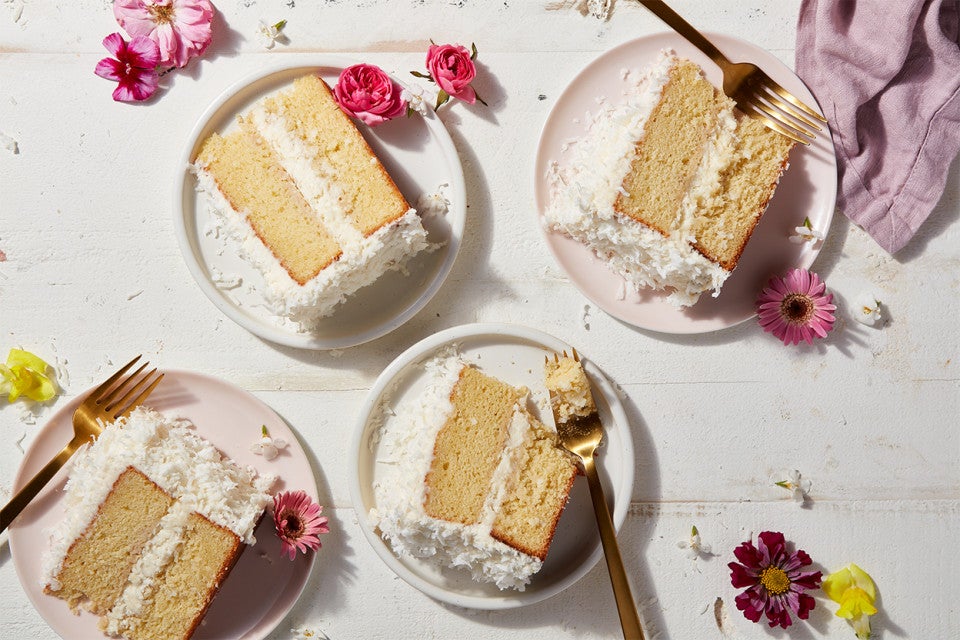 Slices of two-layer Old-Fashioned Coconut Cake on plates, decorated with edible flowers