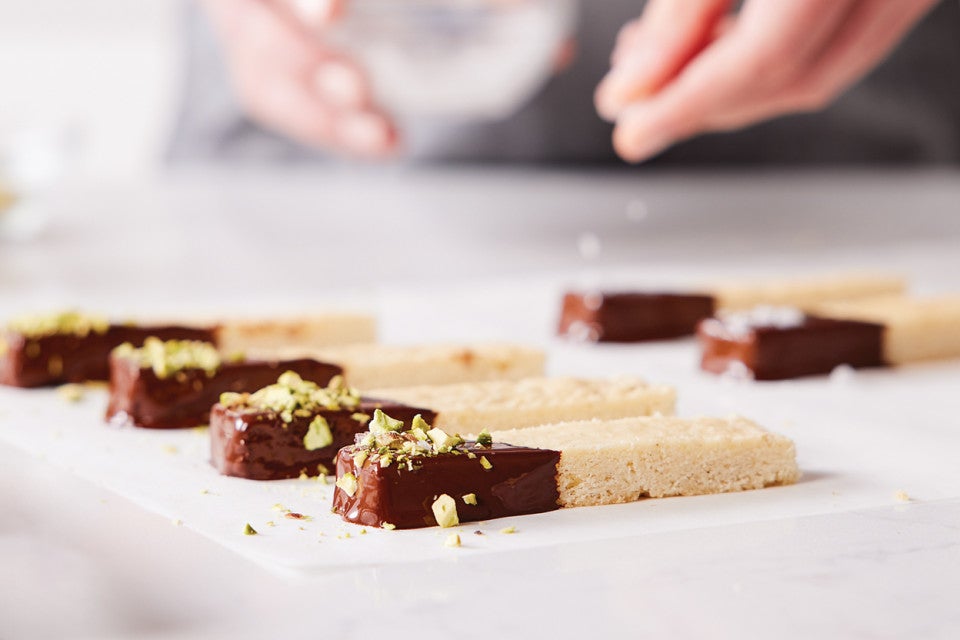 A baker sprinkling salt on top of chocolate-dipped shortbread
