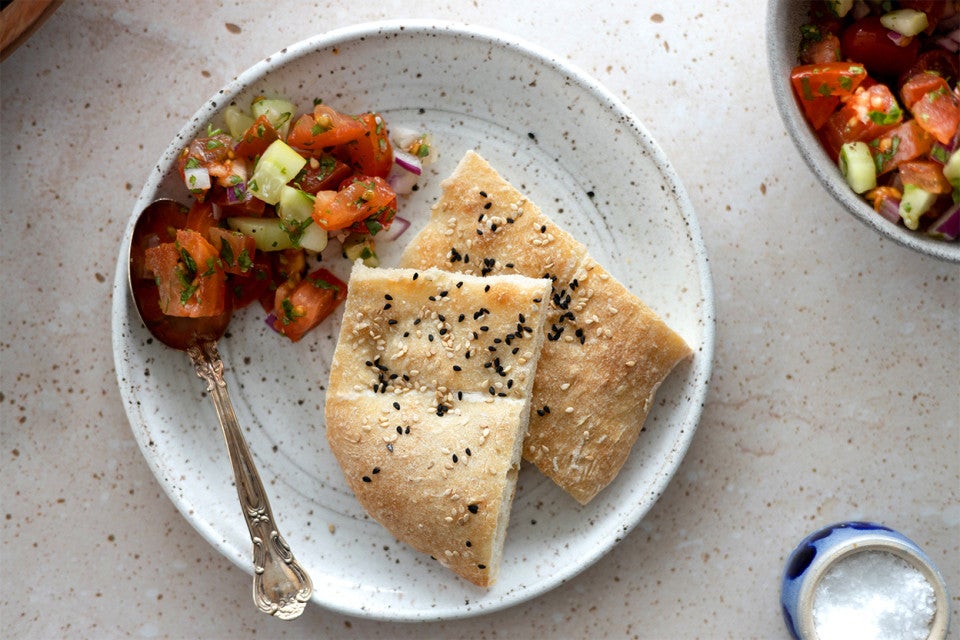 Two slices of Afghan Naan on a plate next to a tomato salad