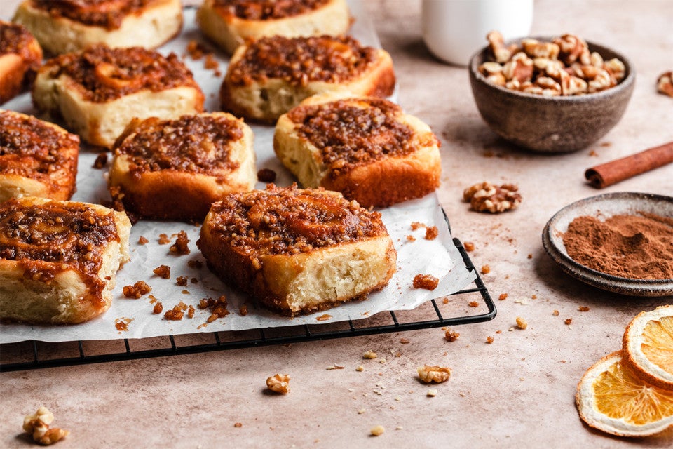 A tray of orange sticky rolls topped with walnuts