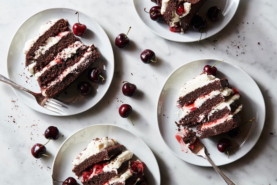 Slice of Black Forest Cake surrounded by fresh cherries, ready to be served