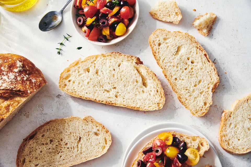 Slices of crusty bread with an even interior crumb structure, alongside a small bowl of chopped cherry tomatoes and herbs.