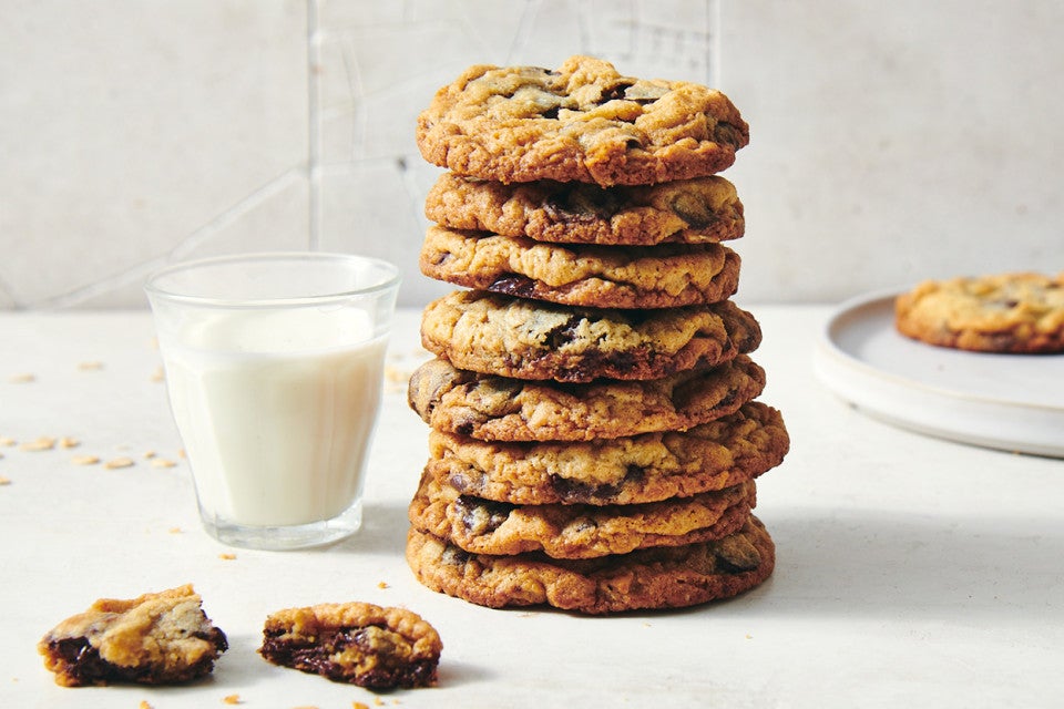 A stack of oatmeal chocolate chip cookies next to a glass of milk. The cookies have crisp golden brown edges and visible chocolate chips.