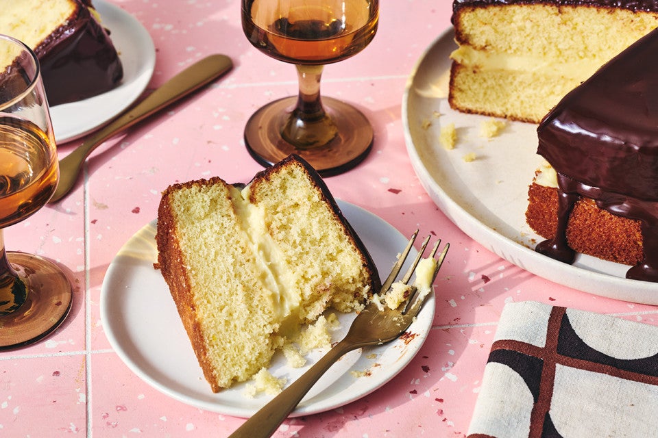 A slice of Boston Cream Pie on a plate with a fork and bite taken out of it.