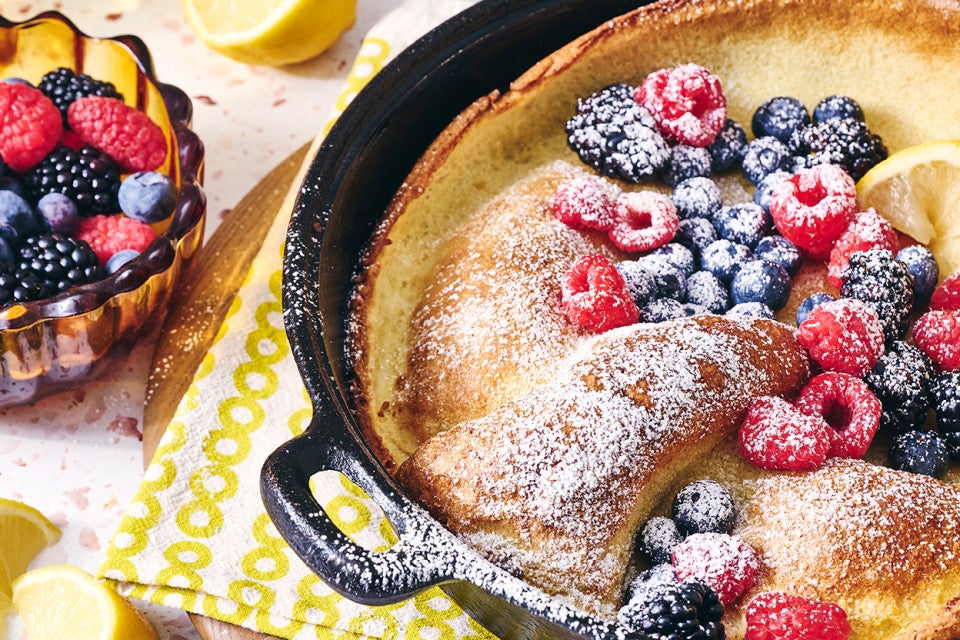 Lemon Puff Pancake with Fresh Berries in a cast iron pan topped with powdered sugar and berries