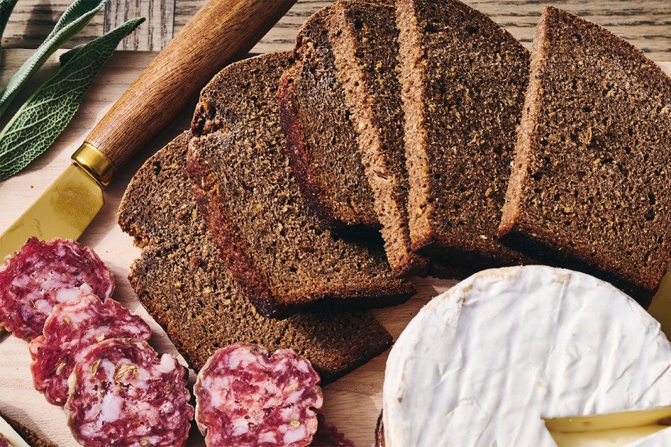 Classic Pumpernickel Bread sliced on a cutting board with meat and cheese