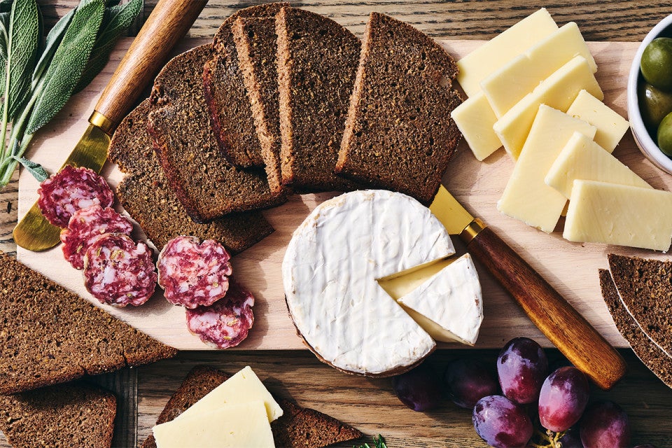 Classic Pumpernickel Bread sliced on a cutting board with meats and cheeses