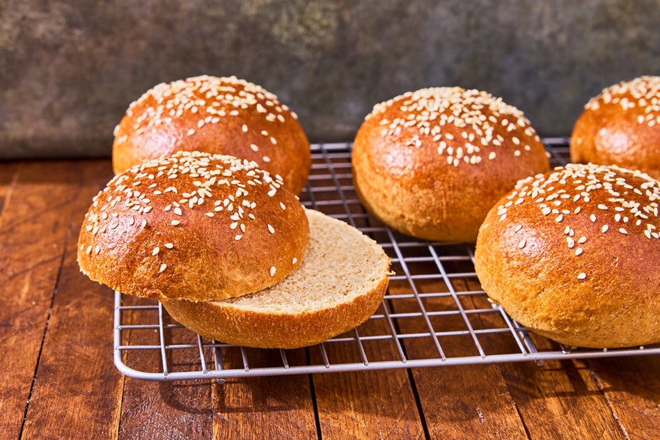 100% Whole Wheat Hamburger Buns on a cooling rack with one sliced