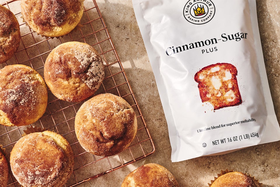 Cinnamon-Sugar Doughnut Muffins on a cooling rack with bag of cinnamon sugar