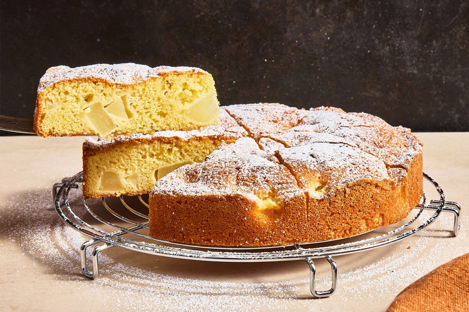 A slice being removed from a Pear and Almond Cake on a cooling rack
