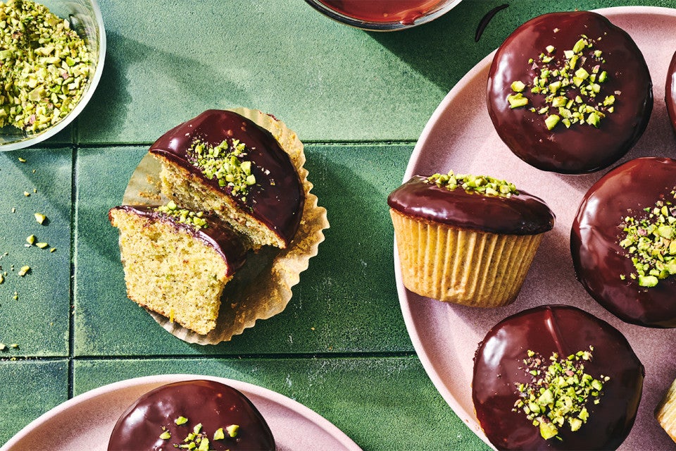 A Pistachio-Cardamom Cupcake with Dark Chocolate Ganache sliced in half and a bunch more on plates