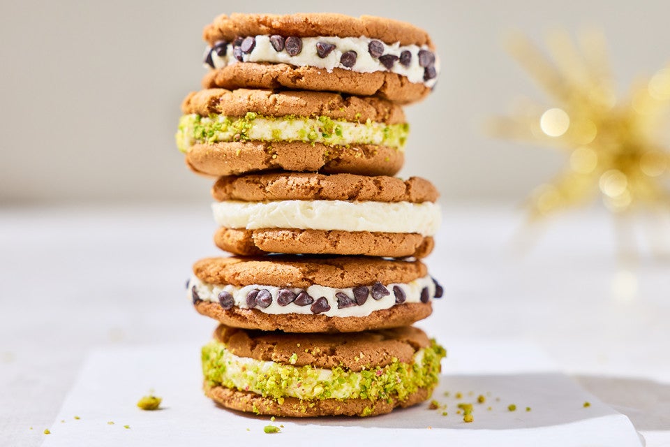 Stacked cannoli sandwich cookies showing the cookies, a layer of filling, and chocolate chips or pistachio coating.
