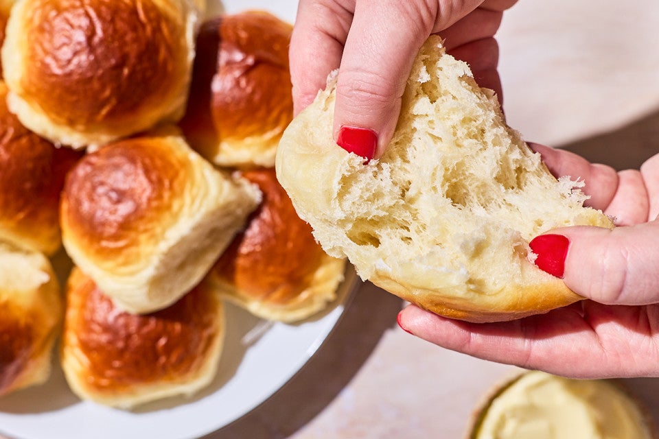 Two hands photographed pulling apart a fluffy homemade dinner roll exposing the airy and moist interior.