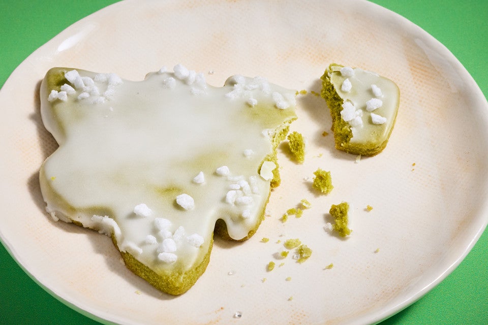 A matcha Christmas tree cookie broken and showing a lovely crumbly green interior on a white plate.