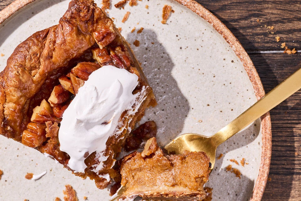 Detailed photograph of a bite of pumpkin pecan pie topped with whipped cream on top of a fork.