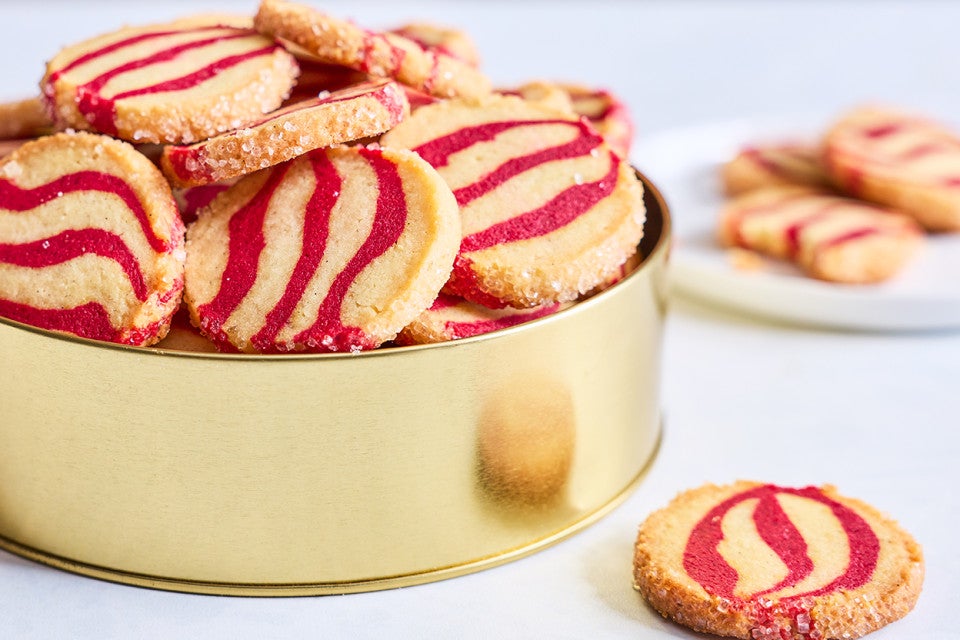 Striped peppermint shortbread cookies inside a gold cookie tin seen from the side.