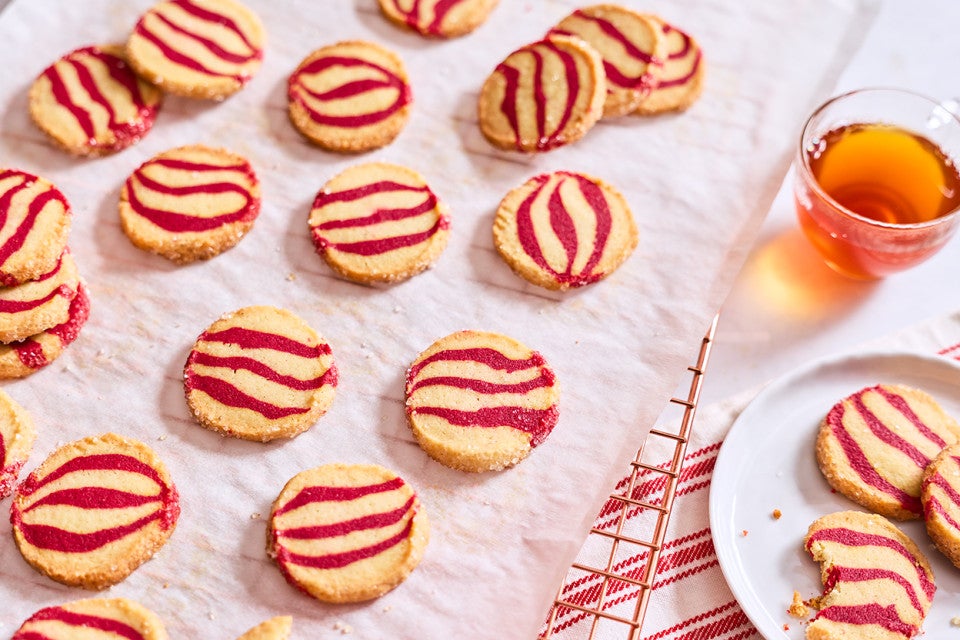 Striped peppermint shortbread cookies laid out on a table with a beverage and plate full of cookies.