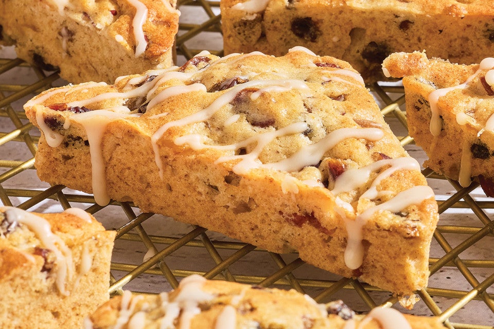 3/4 view of a fruitcake scone showing the glaze drizzled over the top and the edges with a golden brown scone dotted with fruit.