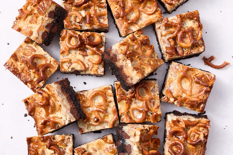 Showing a dozen gluten free chocolate seven layer bars from above with golden hues of caramel and nuts from above.