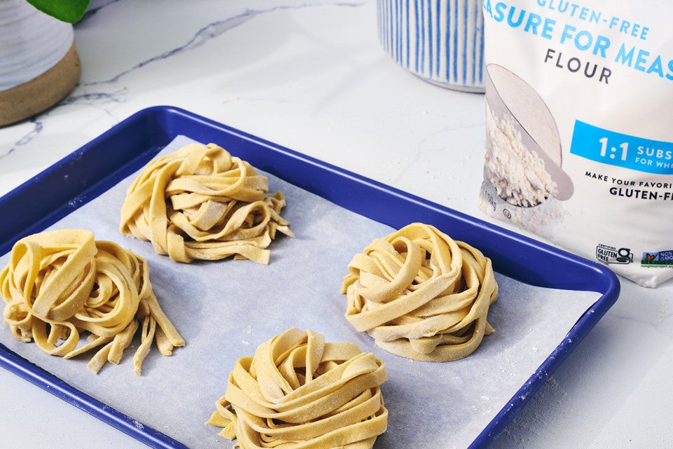 Four balls of raw gluten free pasta sitting on parchment paper on a blue sheet tray.