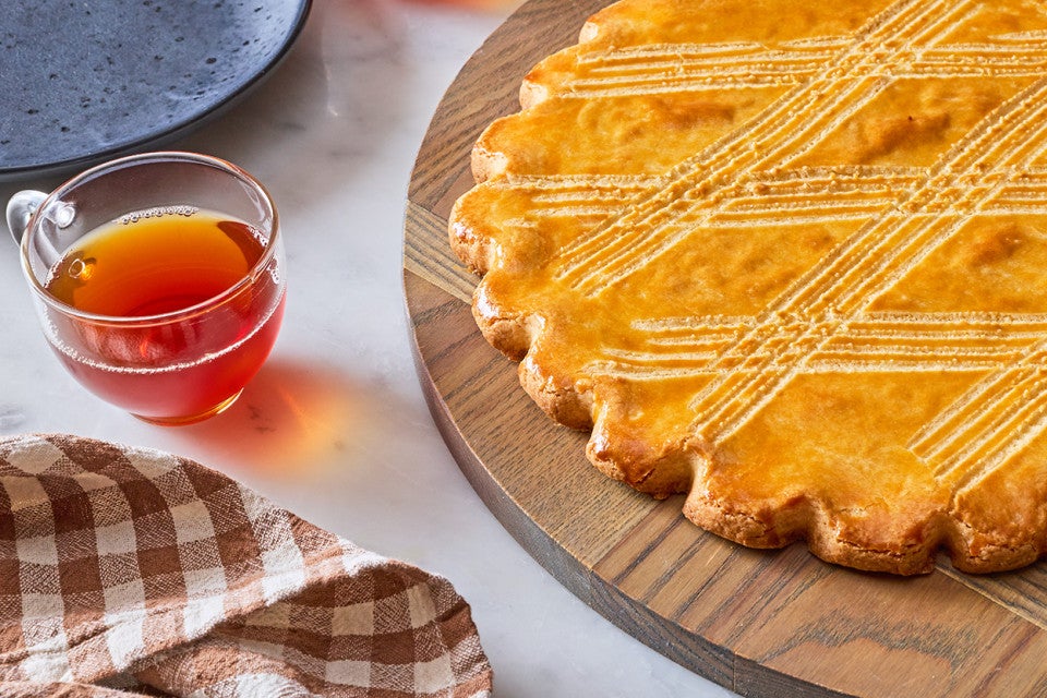 Broyé Du Poitou shortbread from a side angle showing beautifully shaped edges, scoring on top, and a napkin and beverage in the frame.