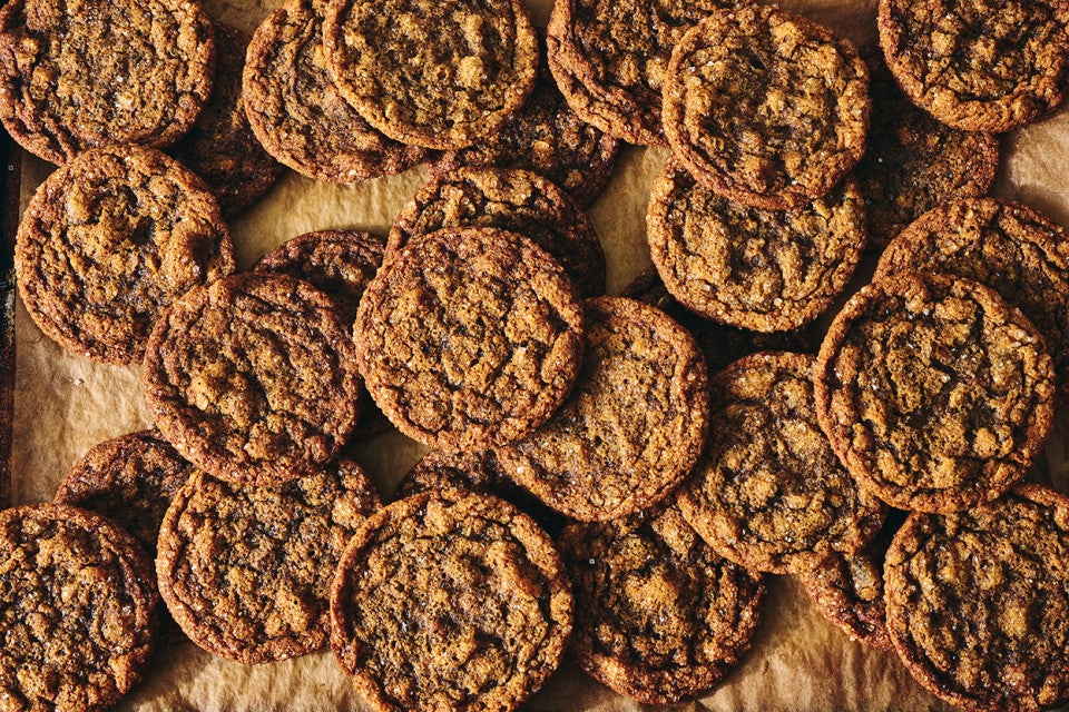 A multitude of Cape Cod Soft Molasses Cookies spread out on dark parchment.