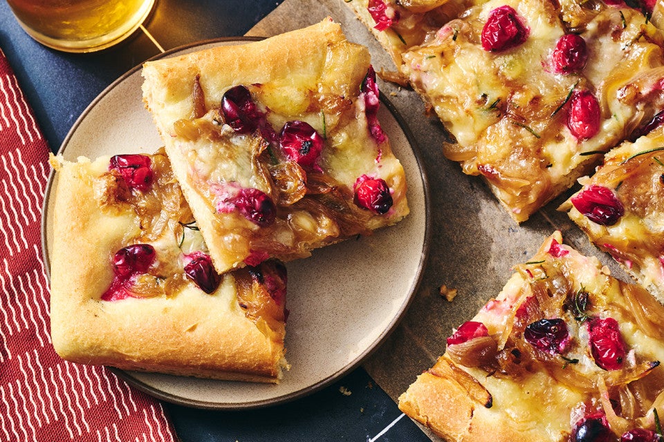 Slices of Caramelized Onion and Brie Pizza on a plate showing a golden baked top dotted with pomegranate, brie, and caramelized onion.
