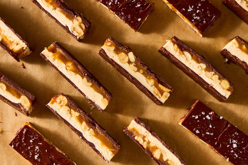 Multiple chocolate peanut nougat bars sliced and arranged on parchment paper showing the layers of chocolate, nougat, caramel, and peanuts.