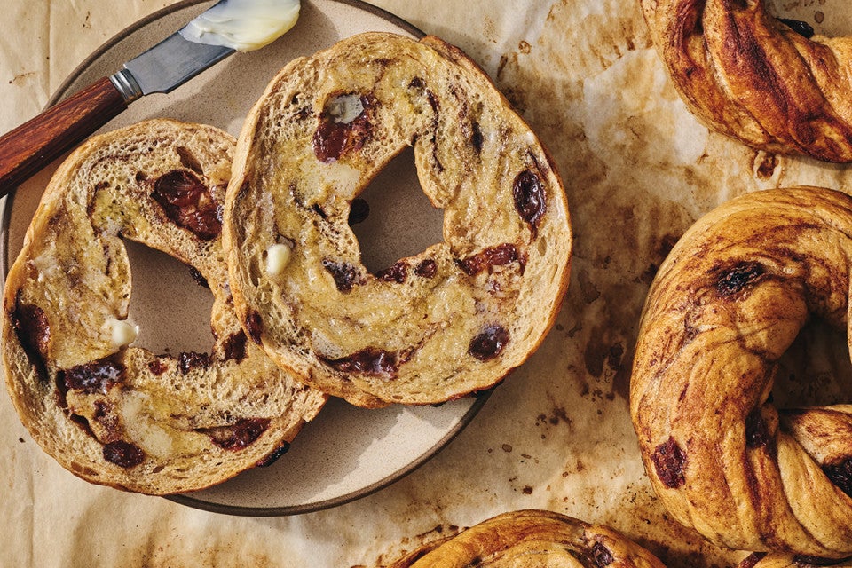 A sliced and buttered Cinnamon Raisin Bagel on a plate.