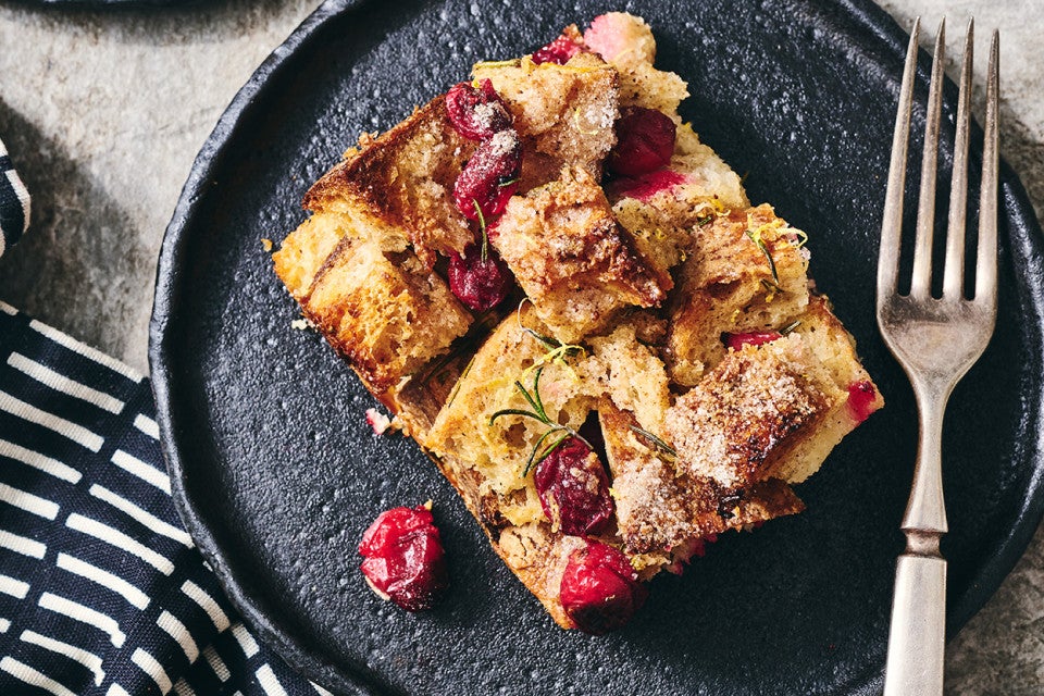 A slice of Cranberry-Rosemary Breakfast Bread Pudding on a dark plate with a fork laying next to it.