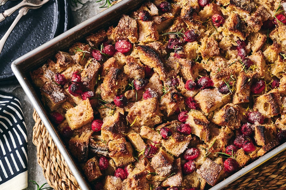 A photograph of the top of Cranberry-Rosemary Breakfast Pudding showing coarsely arranged and baked cranberries, bread, and roesmary.