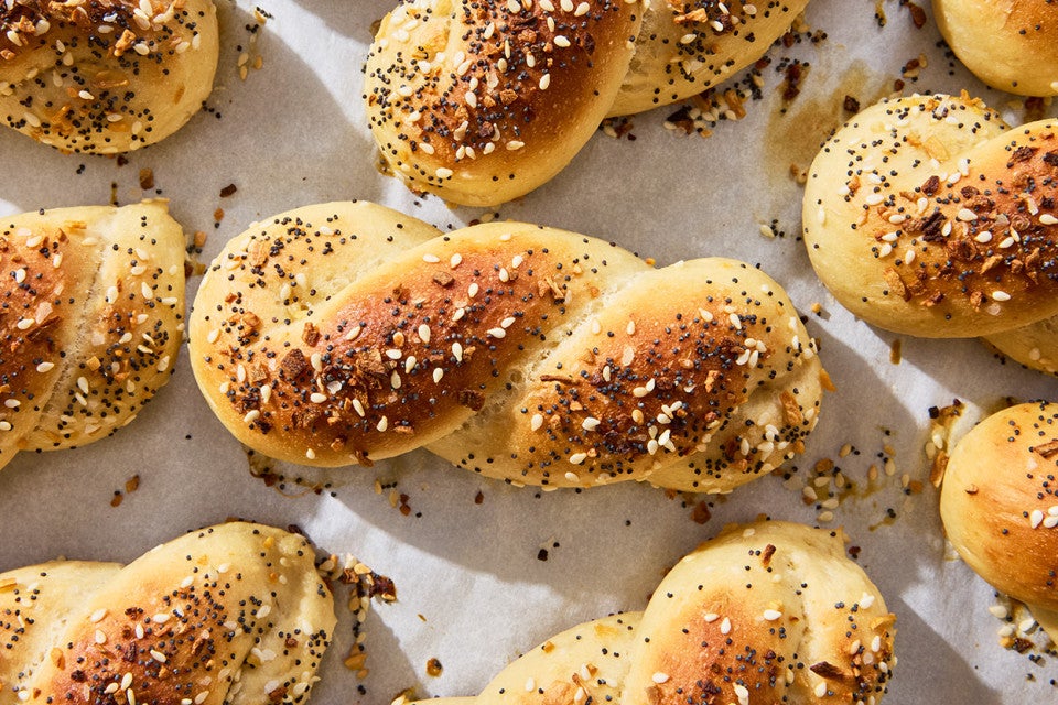 A close up of an Everything Bagel Twist shown fresh out of the oven on parchment with a lovely brown top and bits of everything bagel seasoning.