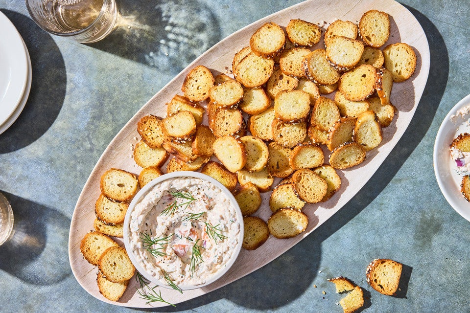 A platter of Everything Bagel Chips spread out around a small bowl of Smoked Salmon Cream Cheese dip.