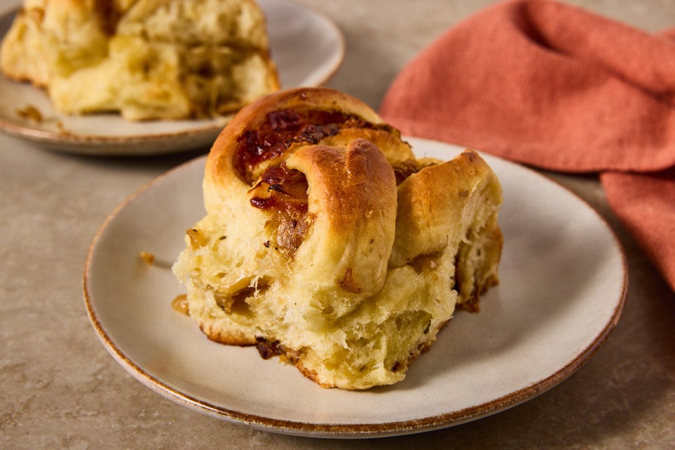 A French Onion Roll on a plate showing the golden brown exterior and lofty baked interior with caramelized onions.