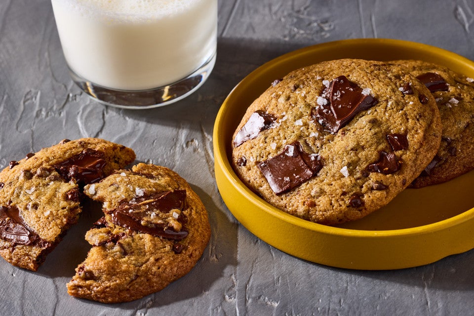 Beautifully baked High-Altitude Chocolate Chip Cookies shown on a plate and counter with a glass of milk in the background.