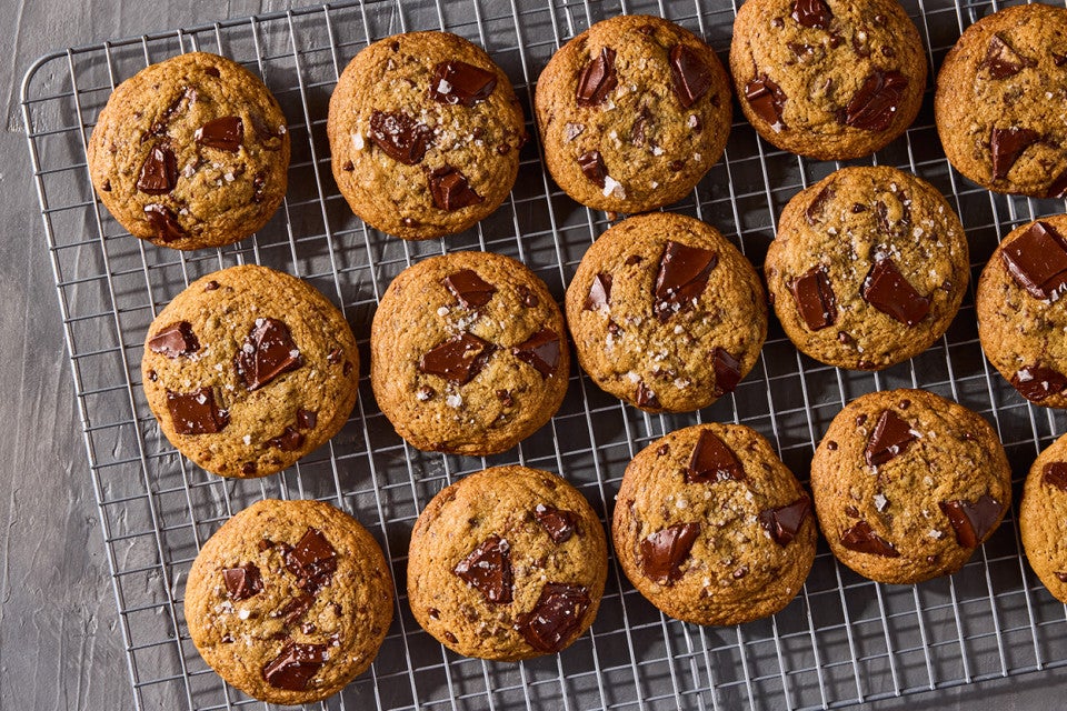 Several beautifully baked High-Altitude Chocolate Chip Cookies shown on a plate and counter with a glass of milk in the background.