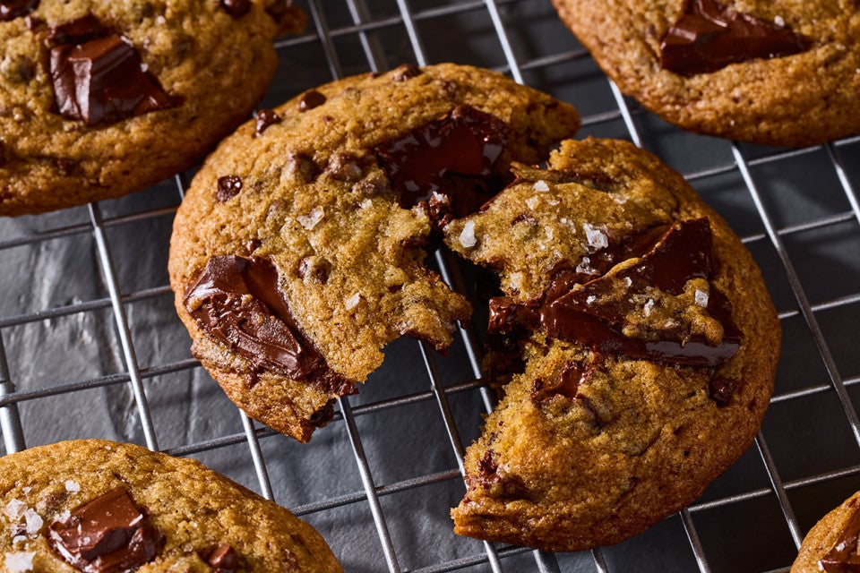 A High-Altitude Chocolate Chip Cookie split on a cooling rack showing the brown color of the dough and the gooey large chocolate bits in the cookie.