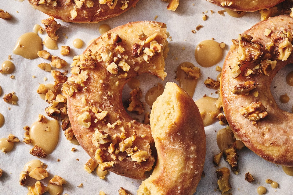 A broke maple donut with a moist and crumbly interior surrounded by dollops of glaze and broken nut meat.