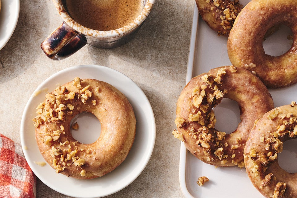 A Maple Donut on a plate with half coated in broke nut meat and the other half glazed.
