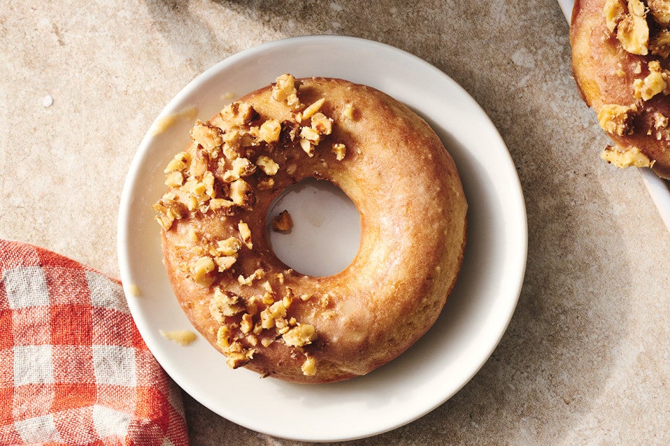 A Maple Donut on a plate with half coated in broke nut meat and the other half glazed.