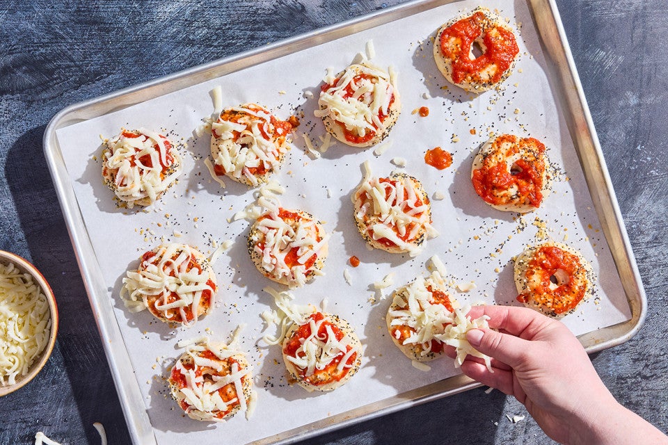 Adding cheese to mini pizza bagels, getting them ready to bake.