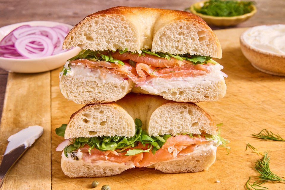 A bagel sandwich sliced in half and stacked with the interior side showing layers of smoked salmon, greens, cream cheese, and a light and chewy bagel interior.