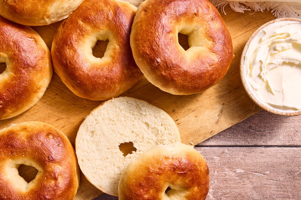 Multiple bagels on a cutting board with one sliced showing the golden interior and perfectly baked brown exterior.