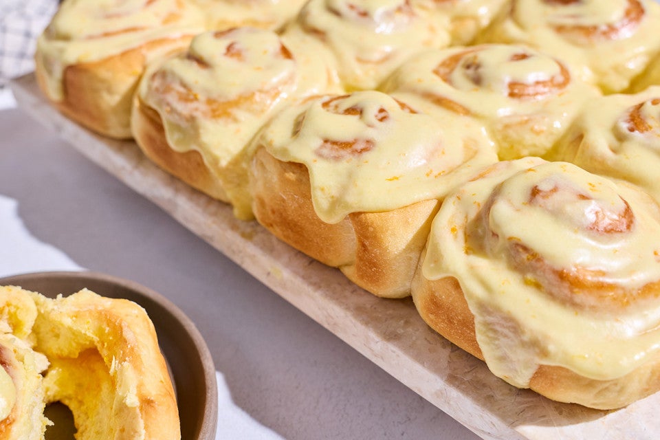 Fluffy Frosted Orange Rolls on a sheet tray showing the side of the rolls with a golden brown and a glossy yellow orange glaze coating them.