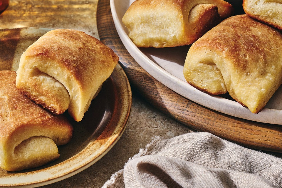 Two plates with Parker House Rolls showing a dark golden exterior and classic fold of the rolls.